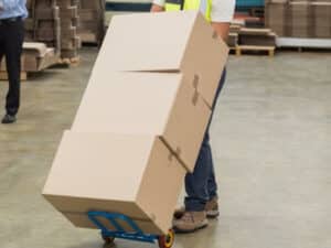 tre scatoloni di grandi dimensioni posizionati su un carrello per traslochi e trasportati da un operatore fuori dal magazzino