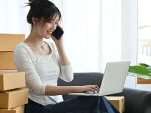 donna al telefono con computer poggiato sullo sgabello e scatoloni trasloco sullo sfondo