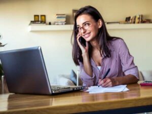 Donna sorridente con gli occhiali davanti al pc e al telefono per contattare fornitore dei servizi